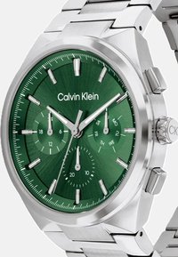 Orologio con quadrante verde e cinturino in acciaio inossidabile argentato. Presenta sottoquadranti cronografici, indici delle ore e marchio posizionato alle 12.