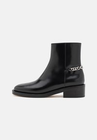 Black leather ankle boot with a glossy finish, block heel, and silver chain accent on the side. Designed for a sleek silhouette.