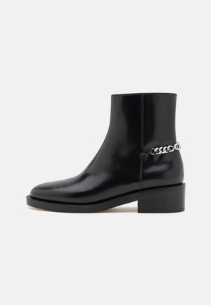 Black leather ankle boot with a glossy finish, block heel, and silver chain accent on the side. Designed for a sleek silhouette.