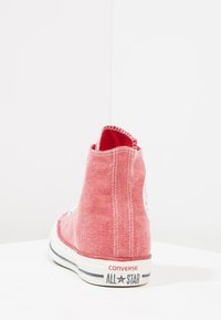 Czerwone płócienne sneakersy typu high-top z kontrastującymi białymi przeszyciami, gumową podeszwą oraz okrągłą łatką z logo na zewnętrznej pięcie.