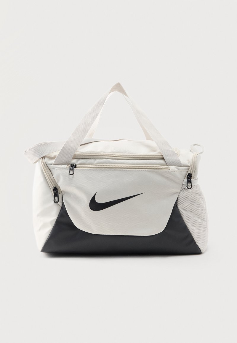 Λευκή και μαύρη τσάντα Nike duffel με επάνω χερούλια, μπροστινή τσέπη με φερμουάρ, πλευρική τσέπη από δίχτυ και μαύρο λογότυπο Nike swoosh μπροστά.