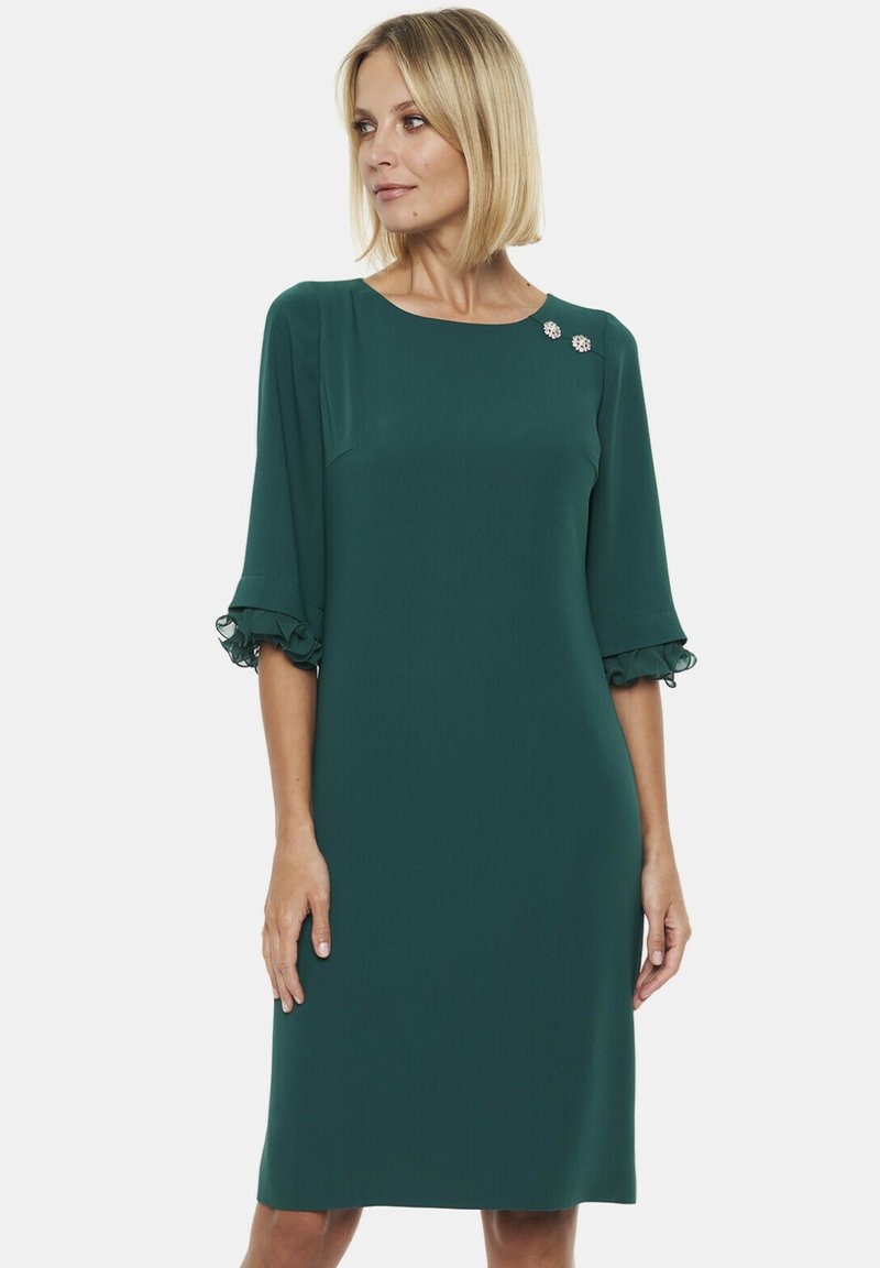 Turkusowa sukienka z trzy ćwiartkowymi rękawami, z falbaniastymi akcentami i dwoma dekoracyjnymi broszkami przy dekolcie. Gładki, lekki materiał.