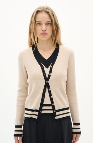 Cardigan beige à côtes avec accents noirs et boutons dorés, présentant un design en V et des poignets et un ourlet rayés. Tissu léger.