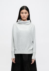 Ανοιχτό γκρι, μαλακό πουλόβερ από πλέξη με λαιμόκοψη και ριγέ τελείωμα, διαθέτοντας μακριά μανίκια και χαλαρή εφαρμογή. Φορεμένο πάνω από μια μαύρη φούστα.