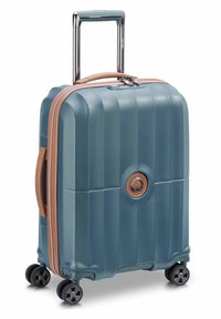 Valigia rigida di colore teal con superficie texturizzata, dettagli color bronzo, maniglia telescopica e quattro ruote multidirezionali.