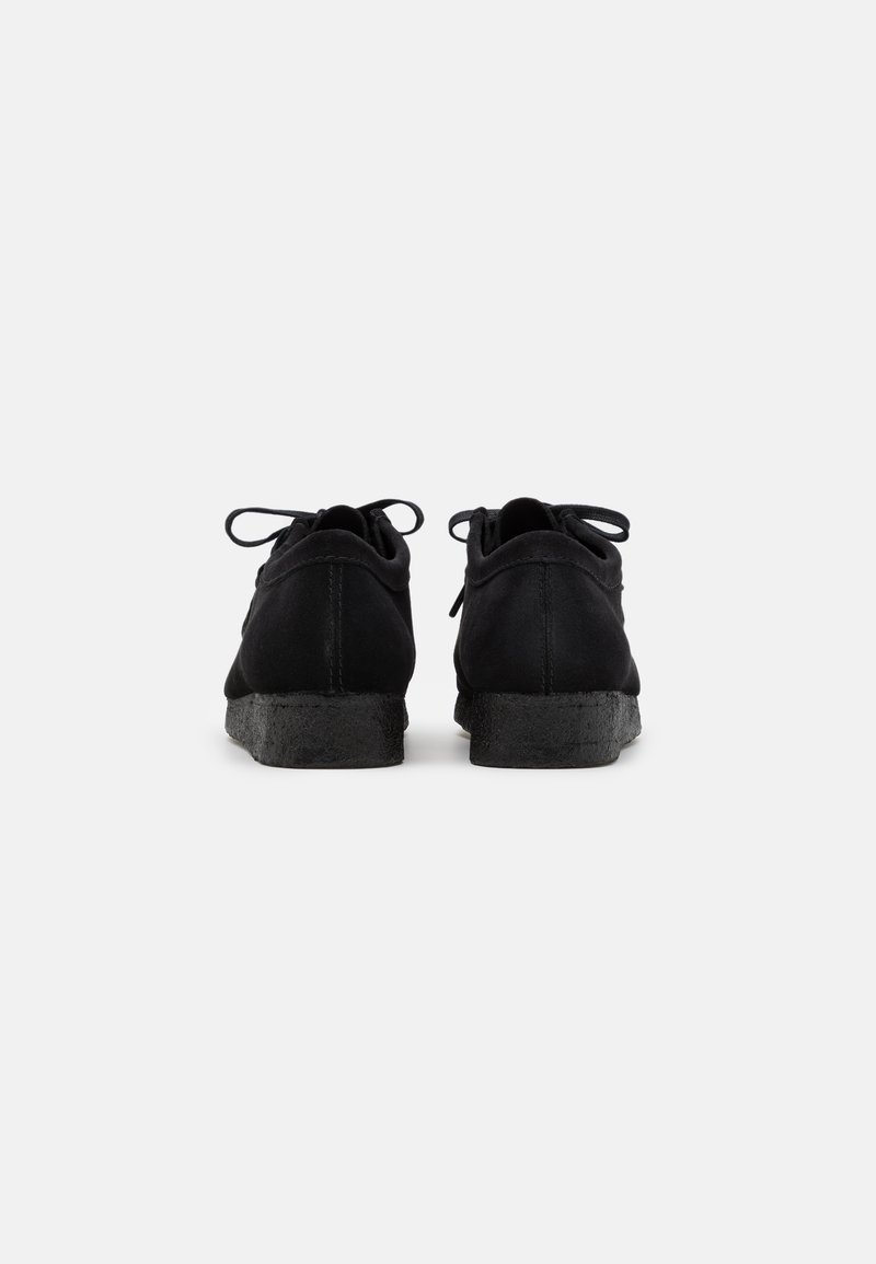 Zwarte suède schoenen met een gevoerde zwarte zool, ronde vorm en striksluiting aan de achterkant. Minimalistisch ontwerp gericht op functionaliteit.