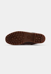 Semelle en caoutchouc d'une botte Timberland marron avec des rainures profondes et un logo embossé au centre, isolée sur fond blanc.