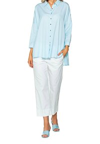 Light blue button-up shirt with a relaxed fit, long sleeves, and a curved hem, paired with white wide-leg trousers and matching slide sandals.