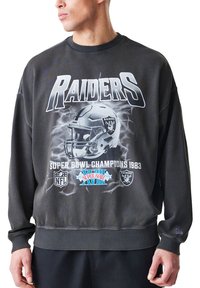 Temno siva majica s krojem okrog vratu, z grafiko Raiders in besedilom Super Bowl 1983. Mehka tekstura, rebrasti manšeti in pas.