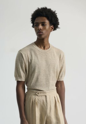 Suéter beige de manga corta con escote redondo, presenta un tejido texturizado. Combinado con pantalones beige a rayas y un cinturón ancho.