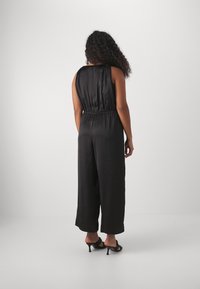 Mono de satén negro con un corte relajado, diseño sin mangas, cintura elástica, pierna ancha y textura suave. La vista trasera muestra un estilo sencillo.