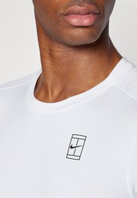 White short-sleeve athletic shirt with a round neck, featuring a small black Nike logo on the left side, made from a textured, breathable material.