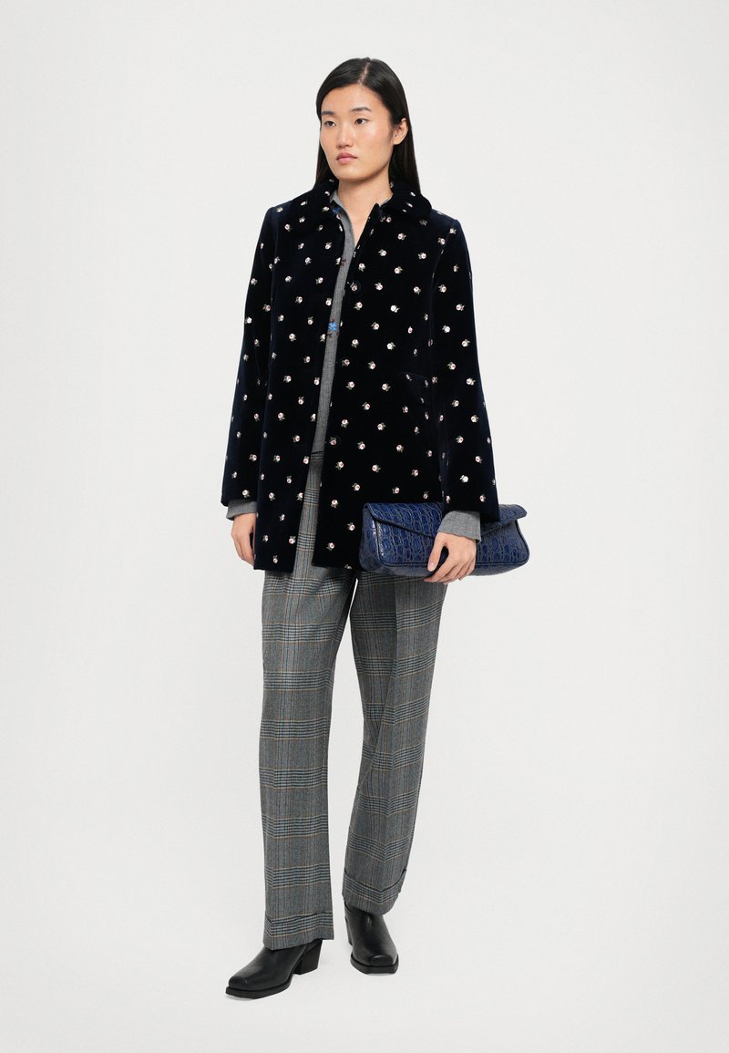 Granatowy aksamitny płaszcz z kwiatowymi zdobieniami, szary długi rękaw, spodnie w kratę i teksturowany niebieski kopertówka. Czarne botki do kostki dopełniają stylizację.