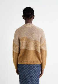 Stickad tröja med rund hals, prydd med beige och bruna horisontella ränder. Strukturen har en texturerad yta med ribbade ärmslut och nederkant.