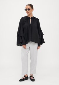 Black, lightweight blouse with ruffled sleeves, keyhole neckline, paired with light grey trousers and black shoes with ankle straps. Sunglasses included.