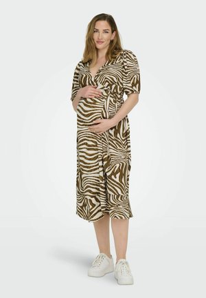 Bruine en witte zebra-gestreepte zwangerschapsjurk met korte pofmouwen en een wikkelontwerp. Draagend met witte sneakers, omarmt het model voorzichtig haar buik.