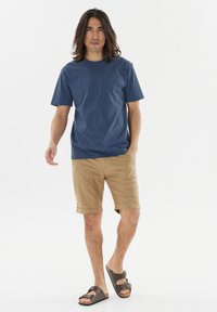 Navyblå bomulls T-shirt i kombination med beiga shorts. Shortsen är uppvikta i fållen. Bruna sandaler fulländar outfiten. Enkelt och avslappnat design.