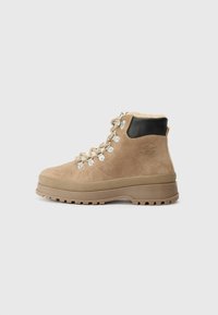 Beige semskede tursko med krage i svart skinn, snørebånd foran, sølvfarget beskyttelse og en tykk, robust gummisåle. Myk fleeceforing synlig.