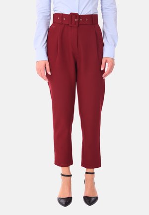 Pantaloni tailorati bordeaux con una cintura larga dotata di una fibbia quadrata, pieghe frontali e lunghezza cropped, abbinati a tacchi neri.
