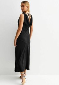 Abito midi nero con scollo a cowl, dettaglio con lacci sulla schiena e silhouette aderente. Tessuto liscio e stoffa fluida si estendono fino all'orlo.