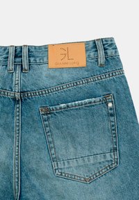 Vaqueros de denim azul claro con una etiqueta de marca de cuero, que presentan costuras acolchadas y un solo bolsillo trasero en el lado derecho.