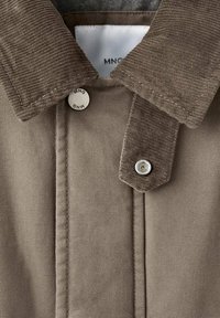 Giacca marrone chiaro con colletto in velluto a costa, bottoni a pressione in metallo e dettagli di cuciture visibili. Tessuto liscio con un design casual.