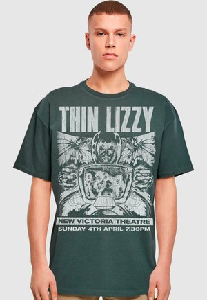 Mørkegrøn bomuld t-shirt med et grafisk print af et hjelme og vinger med "THIN LIZZY" tekst. Løs pasform, rund halsudskæring, korte ærmer.