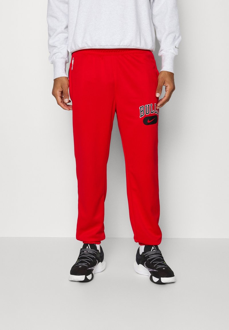 Pantalones jogger rojos con cinturilla elástica, con la palabra 'BULLS' y el logo de Nike en negro. Material suave, corte ajustado y bolsillos laterales.