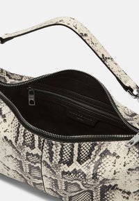 Sac à main en simili cuir beige et noir à motif serpent, ouvert, montrant un intérieur noir avec une poche zippée et une bandoulière.