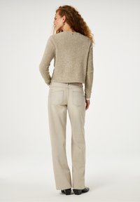 Lichtbeige cropped trui met gestructureerde glitter, gecombineerd met lichtgekleurde slim-fit jeans met studs op de achterzakken.