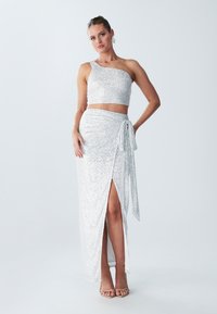 Srebrny, cekinowy, dwuczęściowy zestaw, składający się z topu na jedno ramię i spódnicy w stylu wrap z boku rozcięciem i wiązaniem.