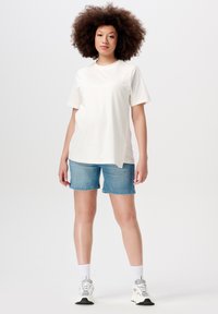 Hvid bomulds t-shirt med korte ærmer og rund hals, parret med midt-blå denimshorts. Hvide sportsko og hvide ankelsokker.