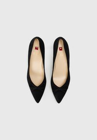 Chaussures à talons hauts en suede noir avec un bout pointu et un petit nœud à l'avant. L'intérieur présente une doublure lisse de couleur nude.