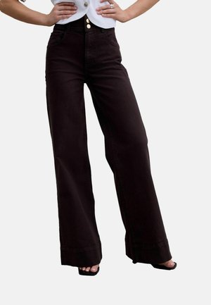 Woman wearing high-waisted wide-leg black pants with double gold buttons, standing with hands on hips, paired with open-toe heels.