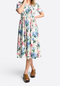 Abito midi floreale con maniche corte, caratterizzato da fiori blu e rosa su uno sfondo crema, abbinato a sandali platform marroni.