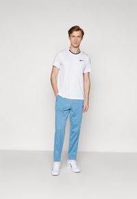 Conjunto deportivo de hombre que incluye una camiseta blanca de manga corta de Nike con logotipo negro y pantalones tapered en azul claro. Zapatillas blancas completan el look.