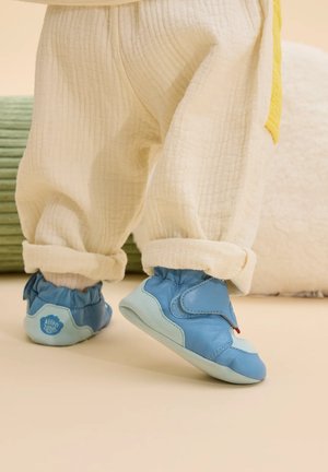 Lichtblauwe zachte leren schoenen met elastische manchet, voorzien van een klittenbandsluiting en een lichtblauwe zool, gecombineerd met crèmekleurige textuurbroek.
