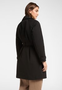 Zwarte trenchcoat met een ceintuur in de taille, kraag en lange mouwen. Soepele textuur en nauwsluitende pasvorm, met een middellange snit.