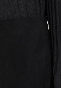 Svart mockabundna tyg med en strukturerad stickad detalj ovanför. Slät yta, kontrasterande texturer och en elegant silhuett utan utsmyckningar.