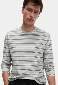 T-shirt grigio a maniche lunghe con righe orizzontali nere, scollo rotondo e maniche arrotolate. Il materiale in cotone offre una vestibilità casual.