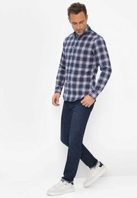 Karierte Hemd in Marineblau und Weiß mit langen Ärmeln, kombiniert mit einer dunklen Jeans und weißen Sneakers. Lässiger Schnitt und strukturierter Kragen.