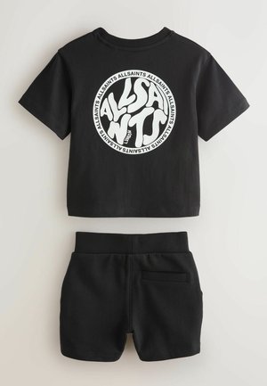 Fekete pamut póló nagy fehér kör alakú logóval; fekete rövidnadrággal párosítva, amely elasztikus derékpánttal és hátsó zsebbel rendelkezik.