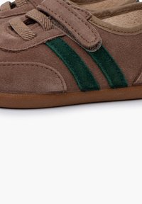 Chaussure en suede marron avec une sangle en velcro, ornée de rayures en suede vert, semelle en caoutchouc plate et doublure intérieure douce.