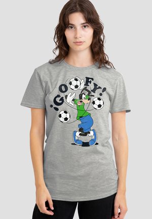 Young woman wearing grey t-shirt with cartoon dog character juggling four soccer balls and text "GOOFY!" on a plain background.