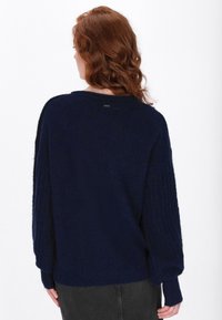 Navy gestrickter Pullover mit langen, gerippten Ärmeln und lockerer Passform. Weicher Stoff, weit ausgeschnittenes Halsbündchen und dezentes Markenetikett auf der Rückseite.