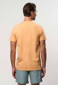 Trumpas rankovėmis, šviesiai oranžinis medvilninis marškinėliai su apskrito kaklo iškirpte; dėvimi su mėlynos ir baltos juostelės šortais, matomais apatinėje krašto dalyje.