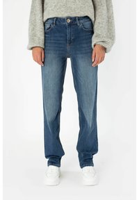 Dámské modré denimové džíny se rovnými nohavicemi, s bledými detaily, pěti kapsami a zapínáním na knoflík, v kombinaci s bílými teniskami.