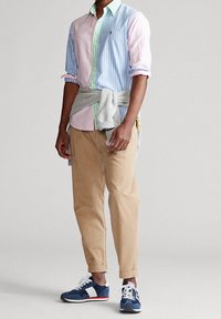 Koszula w paski w wielu kolorach z podwiniętymi rękawami, beżowe chinosy i granatowe trampki z białymi i czerwonymi akcentami. Teksturowany szary sweter związany w talii.