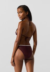 Tumed burgundia bikini komplekt valge lainelise äärisega. Omab kolmnurkset rinnahoidjat ja kõrge vöökohtadega aluspükse, valmistatud siledast kangast.