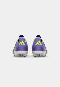Căști de fotbal violete cu accente verzi, având un design elegant, o suprafață texturată și cleats modelate pentru tracțiune și stabilitate.